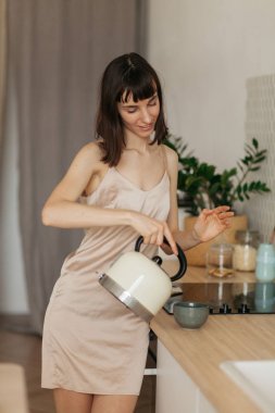 Mutfakta pijamalarıyla gülümseyen bir kız. Güneşli sabahla tanışır. Lezzetli kahve hazırlar.