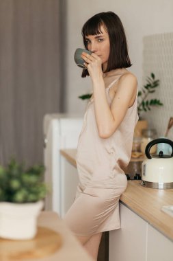 Mutfakta pijamalarıyla gülümseyen bir kız. Güneşli sabahla tanışır. Lezzetli kahve hazırlar.