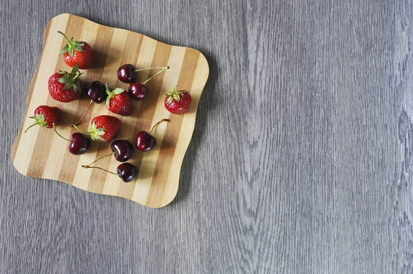 Cherries and strawberries on cutting Board on wooden table