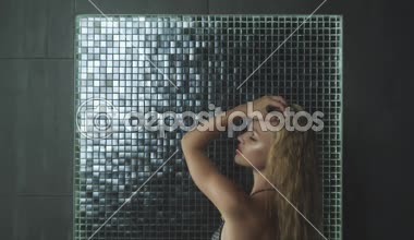 Islak saçlı güzel seksi sarışın kız. Duş su damlaları altında mayoyla poz. Ağır çekim