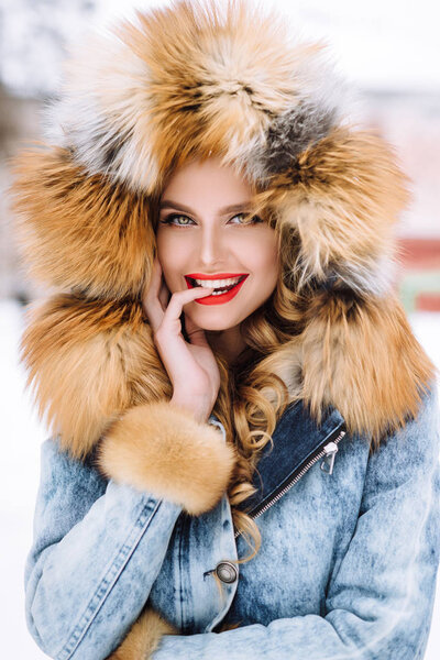 beautiful blonde girl posing in winter fur coat in the snow