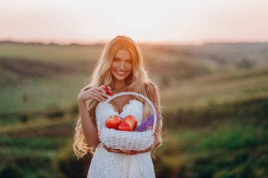 Beyaz elbise güzel seksi sarışın kız meyve sepeti ile günbatımı bir alanda poz 