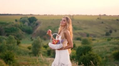 Beyaz elbise güzel seksi sarışın kız meyve sepeti ile günbatımı bir alanda poz 