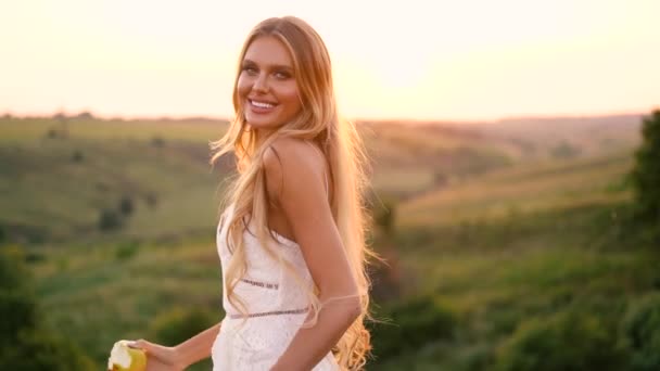 美丽性感的金发女孩在白色礼服在日落时分在田野上摆姿势 一篮子水果 — 图库视频影像