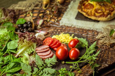  Pizza malzemeleri ve baharatlar ile. Ahşap tahta üzerinde pizza ve çeşitli malzemeler pişirmek. Yeşil fesleğen ve pizza için malzemeler. Yemek yemek için hazır
