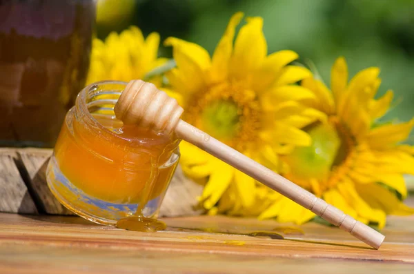 Jar of honey and sunflowers on wooden table over bokeh garden background