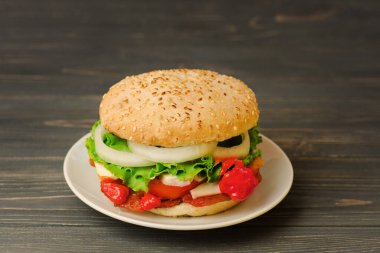 Sosisli sığır burger, marine edilmiş soğan, domates, marul, sos ve ahşap bir tahtanın üzerinde. Koyu, ahşap arka planda Amerikan sığır eti burgerleri. Fast food ya da sokak yemeği konsepti
