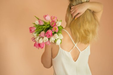 Sarı saçlı, elinde çiçek laleleri olan gülümseyen kız. Baharda elinde pembe lale buketi tutan güzel bir kız.