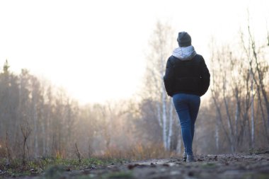 Bahar ormanlarında yürüyen bir kadın. Bahar parkında yürüyorum. Genç bir kadının arka görünüşü.