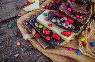 Fındıklı çikolata ve ahşap arka planda kurutulmuş meyve karışımı. Çikolatalar farklı türde çikolatalarla istiflenir. Çikolata parçaları.