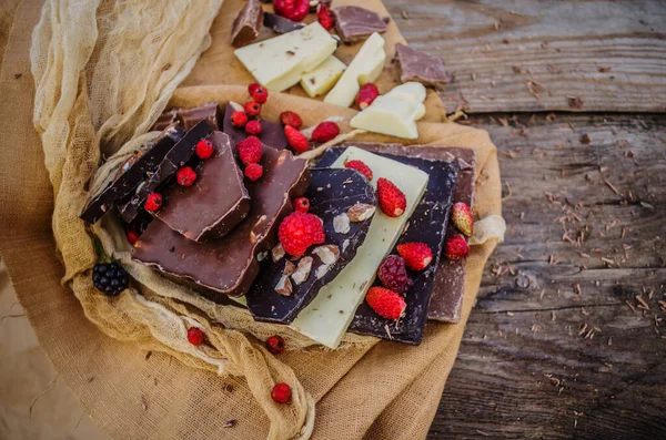 素朴な木の背景にナッツやドライフルーツとチョコレートミックス チョコレートブロックは チョコレートの異なる種類のスタック チョコレートバー作品 — ストック写真