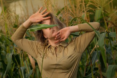 Trendy fashion collection over green corn field plantation. Stylish young woman is standing next corn field behind green leaf plant