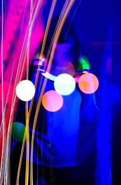 Sahnede, çok renkli arka planda neon ışıkta dans eden sarışın kadın model. Genç, güzel, zarif kız sahnede neon renginde dans ediyor..