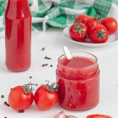 Cam şişede taze domates sosu, beyaz arka planda kırmızı kiraz domatesleri. Yan görünüm.