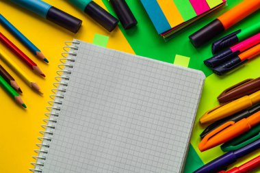 Renkli bir yüzey üzerinde sergilenen canlı kırtasiye öğeleri ve defter, okul hazırlığını, yaratıcılığı ve eğitim temalarını temsil ediyor.