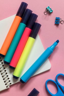Pembe arka planda parlak renkli kalemler ve defter. Okul malzemeleri..