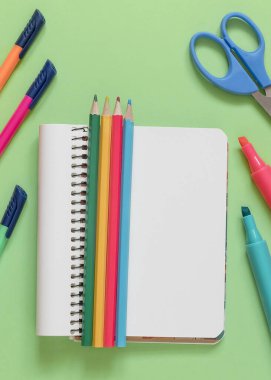 Not defteri, renkli kalemler yeşil arka planda kalemler, kalemler ve makas. Okul konseptine dönelim..
