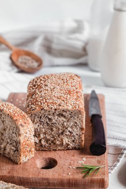 Tahtada taze dilimlenmiş susamlı ekmek, biberiye, bıçak ve süt paçası. Sağlıklı beslenme konsepti. Glütensiz ekmek..