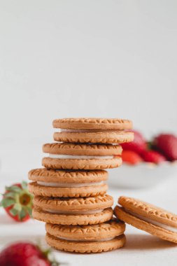 Beyaz bir masada taze kırmızı çilekli bir yığın tatlı sandviç kurabiyesi..