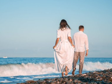 Birbirine aşık bir çift kumsalda beyaz elbiseler içinde koşuyor..