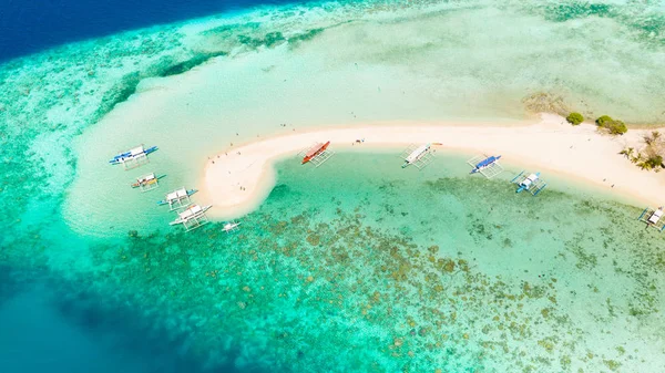 Ditaitayan adasında beyaz kumlu plaj. Adada tekneler ve turistler.