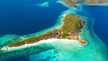 Ditaitayan adasında beyaz kumlu plaj. Adada tekneler ve turistler.