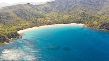 Turkuaz su ve küçük beyaz plaj ile deniz koyu. Güzel lagün ve volkanik ada yoğun orman ile kaplı, yukarıdan görünümü.