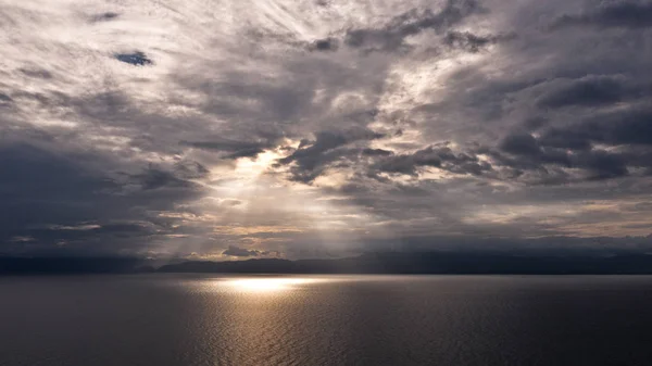 Clouds and rays of sun above the sea. Bright light with sun rays and heavy clouds above the sea. Dramatic sky.