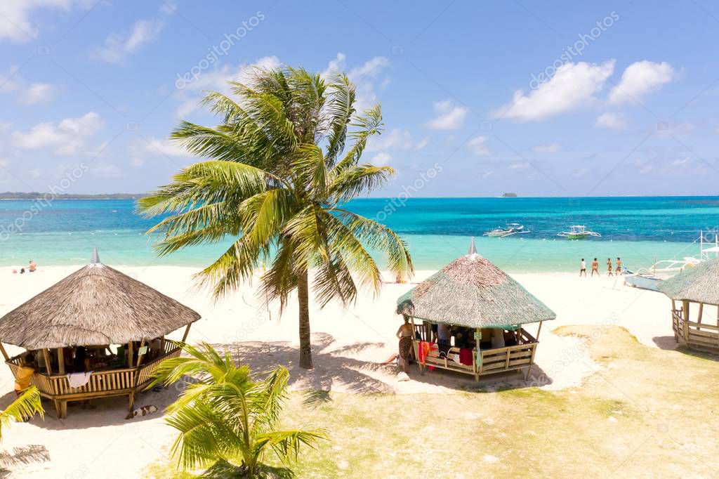 Daco island, Philippines. Palm trees and bungalows on the white sandy beach. People relax on a tropical island.