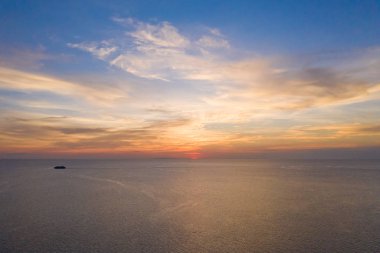 Deniz üzerinde gün batımı ve uzakta yelkenli gemi.