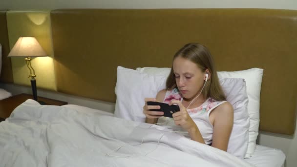 Chica en la cama con un teléfono inteligente en sus manos — Vídeo de stock