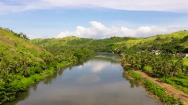 Büyük bir tropikal adada kırsal alanda. Nehir kenarındaki yeşil tepelerde küçük bir köy. Filipinlerin doğası, Samar.