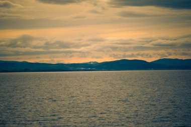 Gün batımında dramatik bulutlarla manzaralı deniz ve dağlar