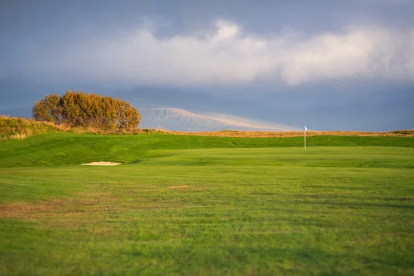 Golf sahası yeşil bayrak ve dramatik bulutlu gökyüzü, İzlanda