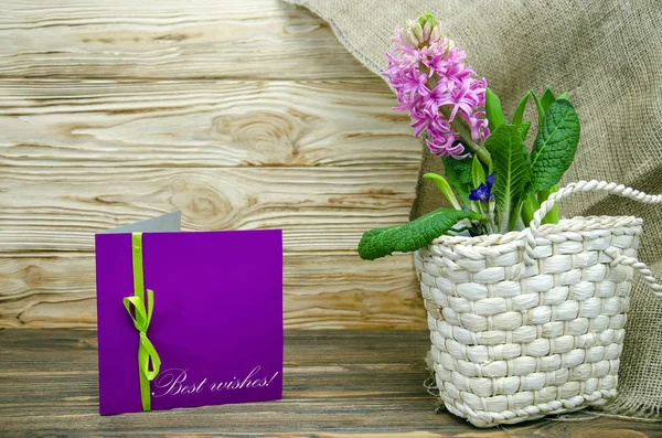 Best wishes.Greeting card on a wooden background and a hyacinth flower in a decorative flower pot in the form of a basket.