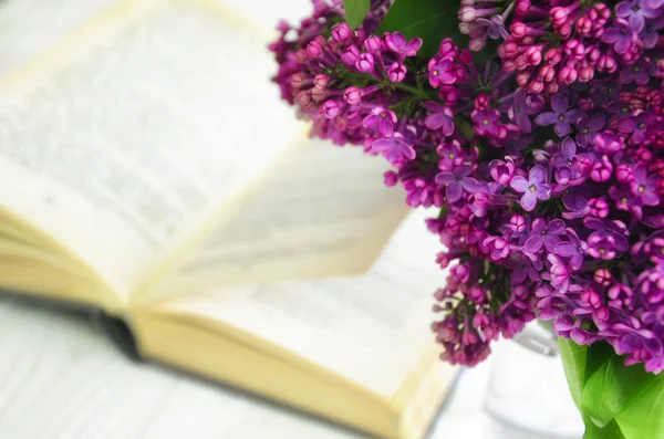 Lilac and a book. A bouquet of spring flowers against the background of an open book lying on a white wooden surface.