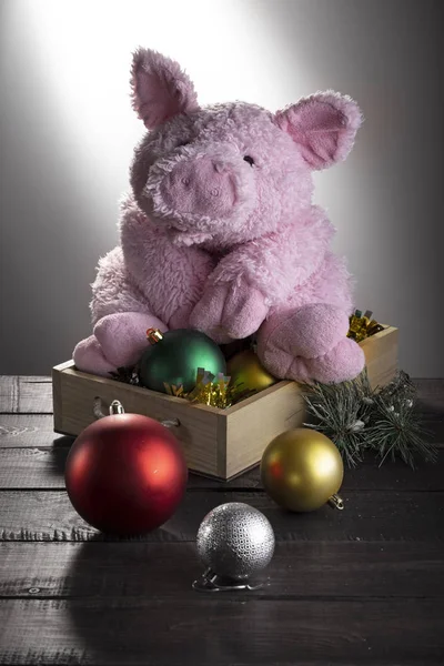 Toy pig sitting on box with New year balls on wooden surface. Festive card, Chinese New Year of Pig, Zodiac symbol 2019