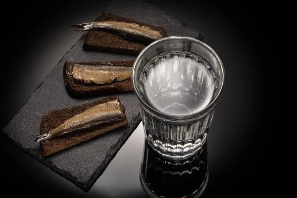 Ποτήρι με αλκοόλ και ορεκτικό με παπαλίνα (σαρδελόρεγγα) και ψωμί στο πέτρινο πιάτο. — Φωτογραφία Αρχείου