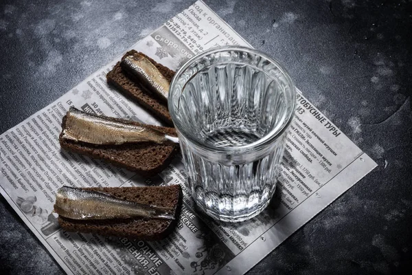 Ρωσική ακόμα-ζωή με αλκοόλ, Ρωσία - 23 Φεβρουαρίου, 2019: γυαλί με βότκα και σνακ με παπαλίνας και τα ψωμί σε παλιά εφημερίδα. — Φωτογραφία Αρχείου