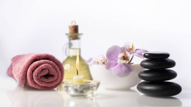Spa natürmort kompozisyon beyaz arka plan üzerinde. Havlu, yanan mum, yağ ile şişe ve yay çiçek ile yanındaki Zen spa taşlar.