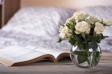 Hafif rahat yatak odası iç başucu masada gül ve kitap ile cam vazo.