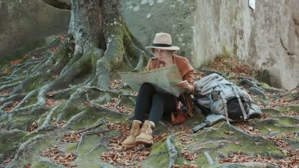 Mujer joven con elegante sombrero y camisa mirando al mapa turístico, a continuación, mirando a su alrededor. Al aire libre . — Vídeos de Stock