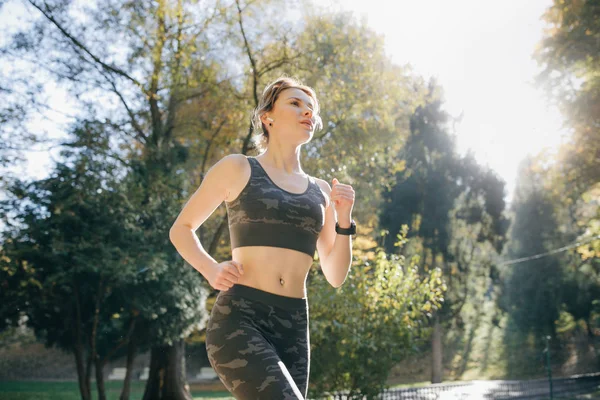 Portrait d'une jolie coureuse brune qui court dans les aéropodes du parc urbain écouteurs bluetooth. Fitness santé femme athlétique jogging en plein air — Photo
