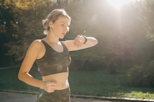 Femme de remise en forme dans les écouteurs sans fil en utilisant Smartwatch et court dans la lumière du matin — Photo