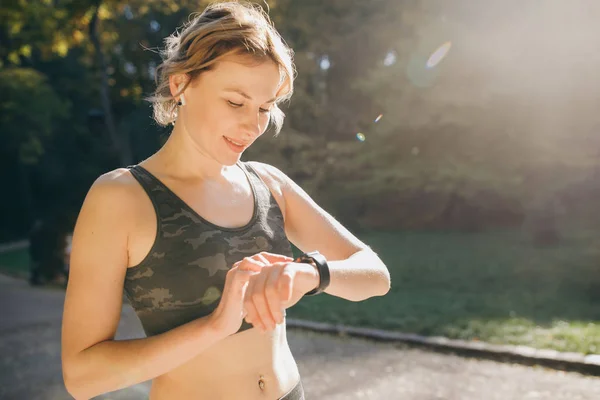 Mujer Fitness Con Auriculares Inalámbricos Usando Smartwatch y funciona con luz de la mañana — Foto de Stock