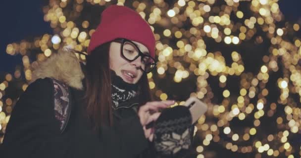 En ung kvinne som bruker smarttelefon i en overfylt gate. Hun sjekker e-poster, samtaler eller nyheter. By om natten . – stockvideo