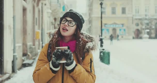Chica con café en sus manos camina por las calles de una ciudad nevada — Vídeos de Stock