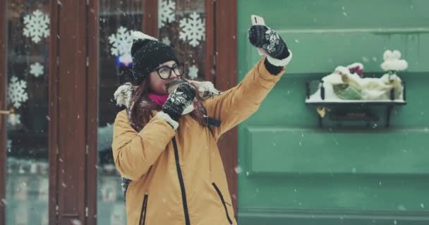 Smiling girl makes selfie on a background of snowy in a winter city street — Stock Video