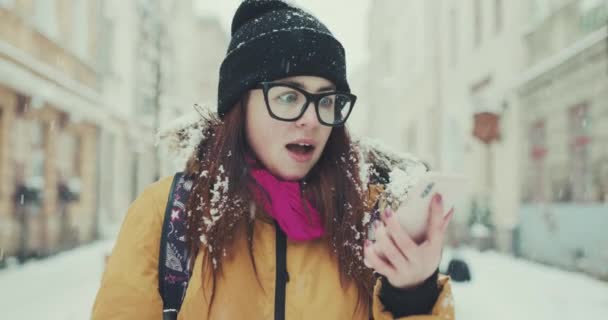 Vista frontal de uma mulher animada, verificando o telefone e celebrando boas notícias em uma rua da cidade de inverno — Vídeo de Stock