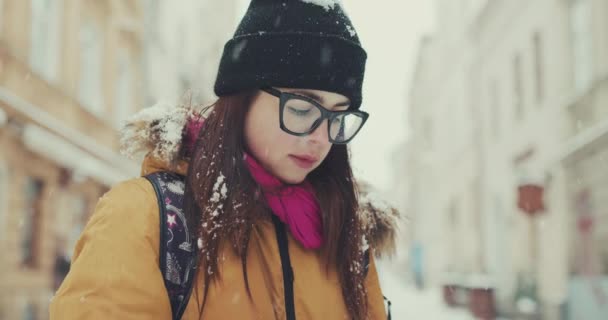 Une jeune femme en tenue tendance se promène dans la ville hivernale en passant par les cafés locaux, les SMS via son téléphone, en naviguant sur Internet. Utilisation de la carte en ligne, gps . — Video